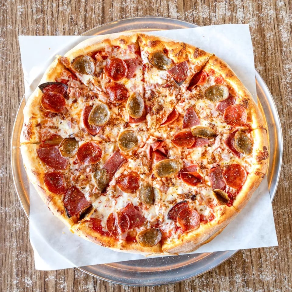 A whole meat lover's pizza with pepperoni, sausage, and bacon on a metal pan.