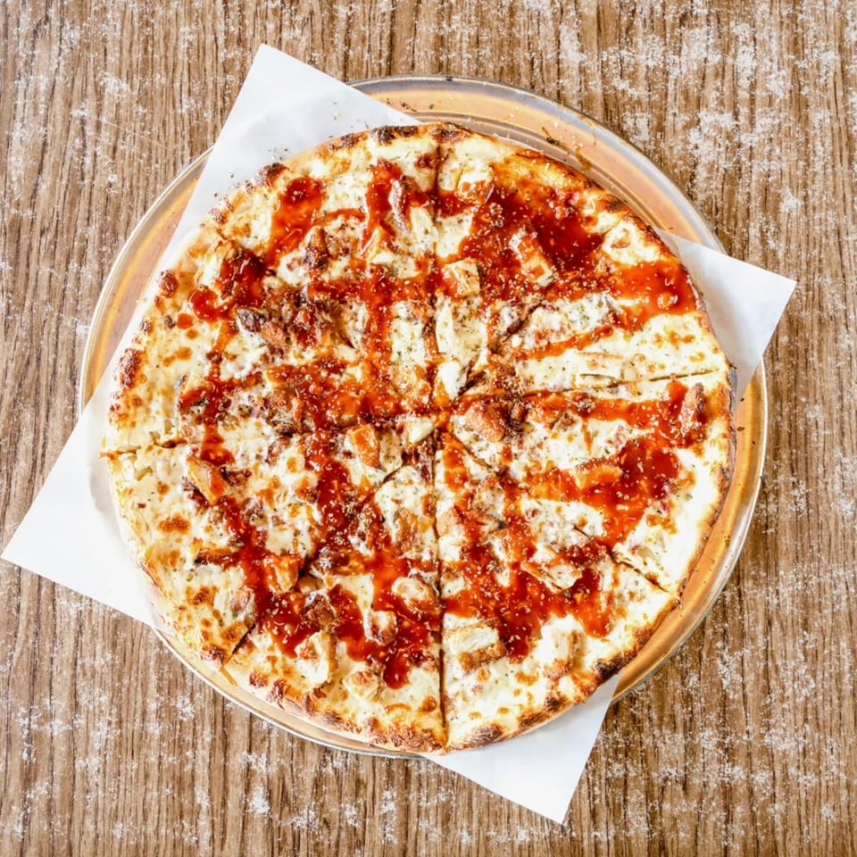 Top-down view of a whole BBQ chicken pizza, sliced, on a metal pan and wooden table.