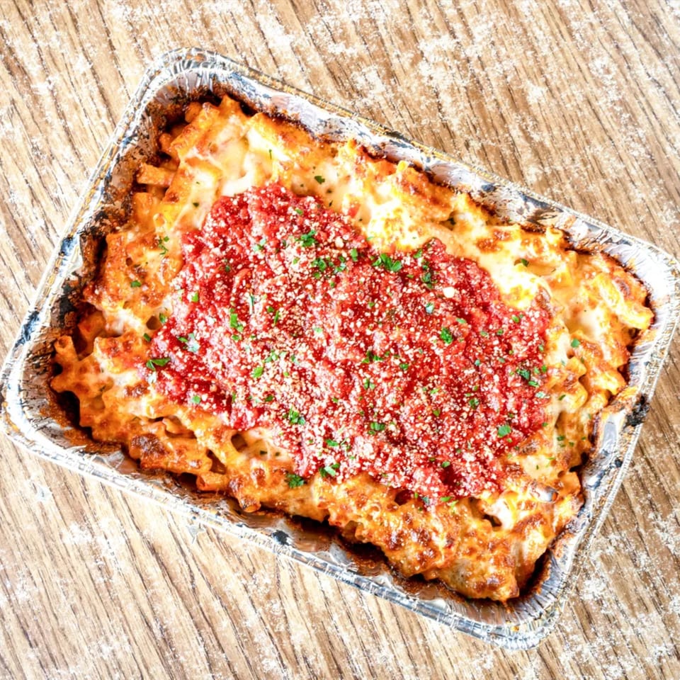 Baked ziti with melted cheese, red sauce, and parsley in a foil pan on a wooden table.