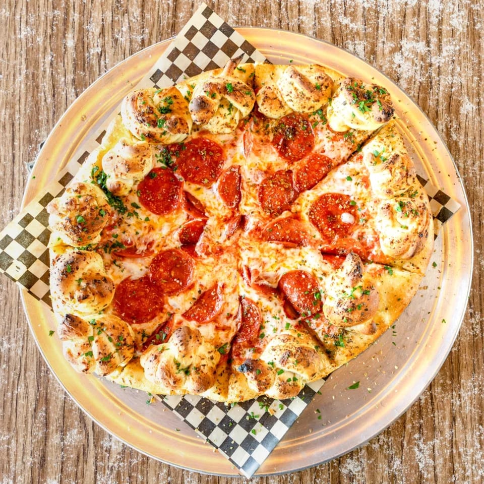 Pepperoni pizza with garlic knot crust, served on a metal tray with checkered paper.
