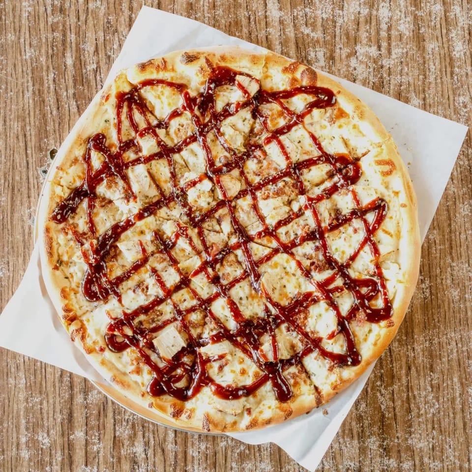 Overhead view of a BBQ chicken pizza with a lattice of sauce on a wooden table.