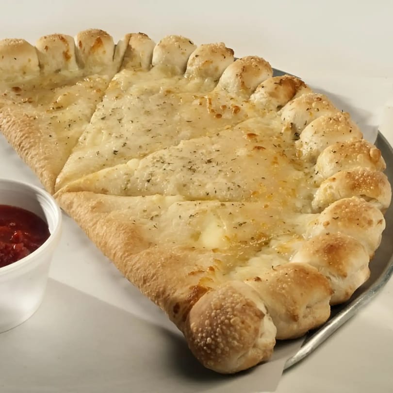 A large, cheesy calzone with a braided crust and a side of marinara sauce.