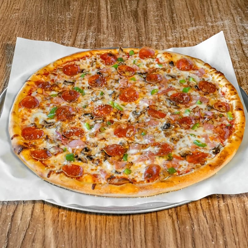 A whole pepperoni, mushroom, and green pepper pizza on a metal tray with parchment paper.